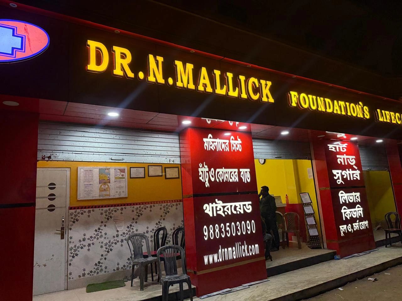 Dr. N. Mallick Foundation's healthcare clinic illuminated at night with seating outside.