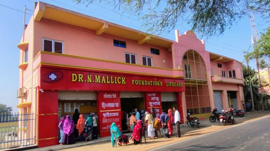 People gathered outside Dr. N. Mallick Foundation's Lifecare building on a sunny day.