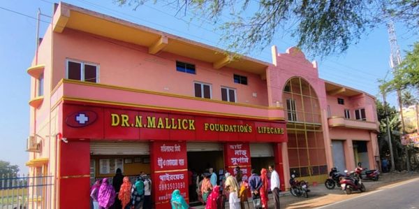 People gathered outside Dr. N. Mallick Foundation's Lifecare building on a sunny day.