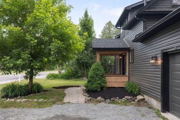 Modern black house exterior with greenery and stone path.