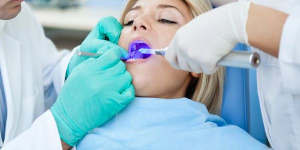 Dentist treating a woman with dental tools and blue curing light.