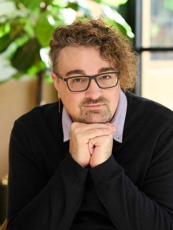 Person with curly hair and glasses resting chin on hands.