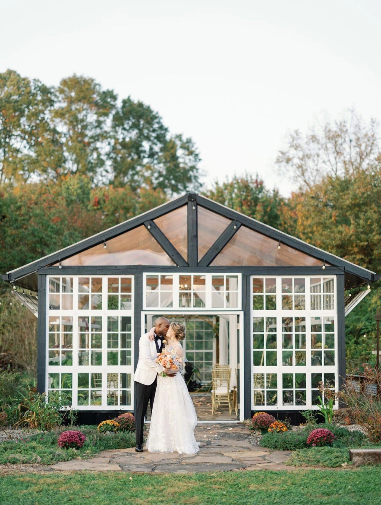 Couple standing in front of Greenhouse front facing with brick pathway leading to entrance,
Photo by