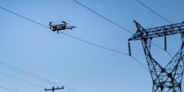 A drone flying near electrical power lines under a clear blue sky.