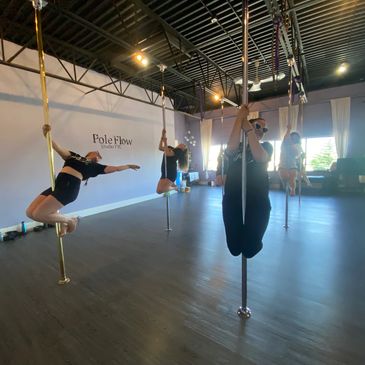 Women practicing pole dancing moves in a studio named Pole Flow.