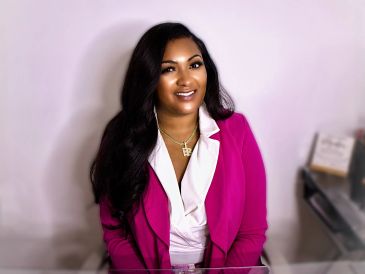 Woman smiling, wearing pink blazer and white blouse.