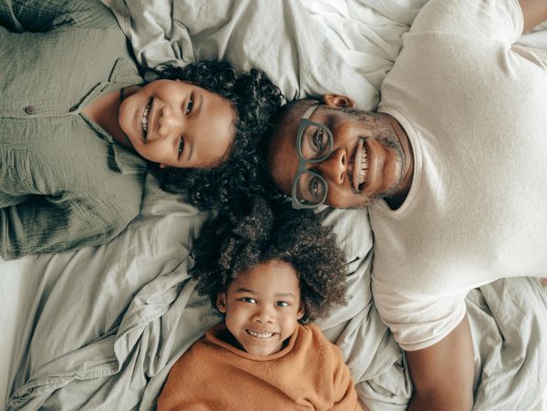 Smiling father and two children lying on a bed, enjoying a happy moment together.