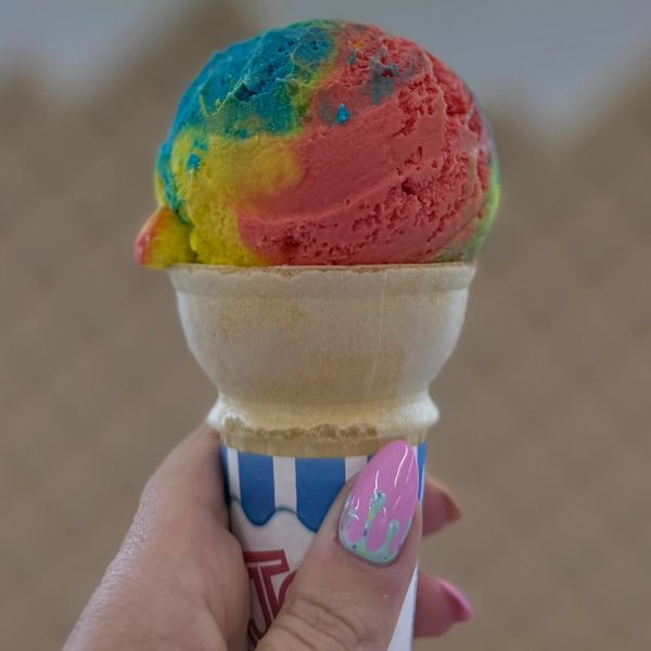 Hand holding a colorful rainbow ice cream cone with pink nail art.