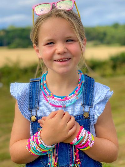 Smiling girl wearing colorful bead necklaces and bracelets outdoors.