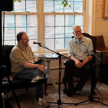 Two men seated indoors, engaged in conversation with microphones.