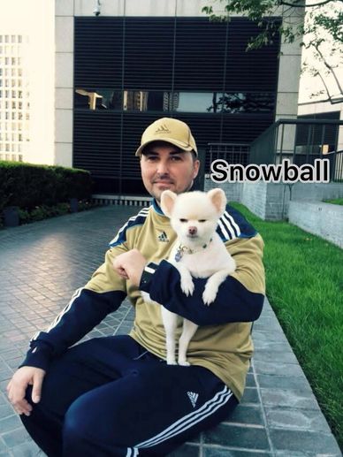 Man sitting with a small white dog named Snowball on his arm outdoors.