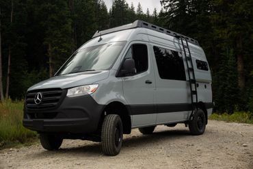 A gray Mercedes-Benz camper van parked on a dirt road in a forest.