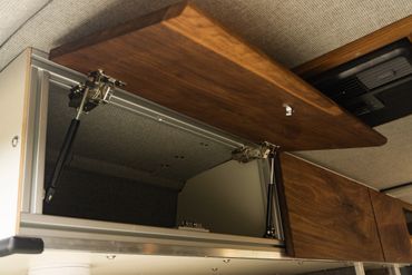 Open overhead wooden cabinet with hydraulic hinges inside a vehicle or small space.