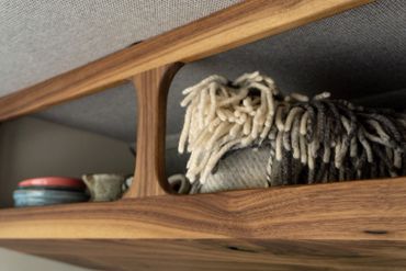 Close-up of wooden shelf holding folded blankets and ceramic dishes.