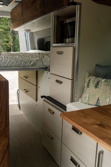 Compact camper van interior with bed, storage drawers, and wooden accents.