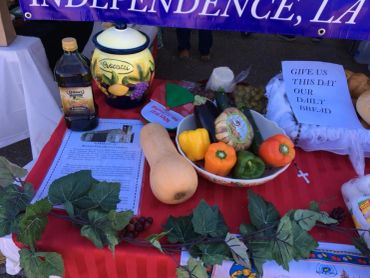A table display with vegetables, a jug, and a sign with a prayer quote.