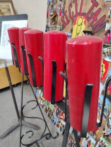 A row of tall red candles in black metal holders.