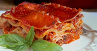 A slice of pepperoni lasagna on a plate with basil.