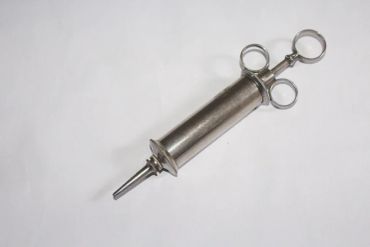 Vintage metal syringe with finger rings on a white background.