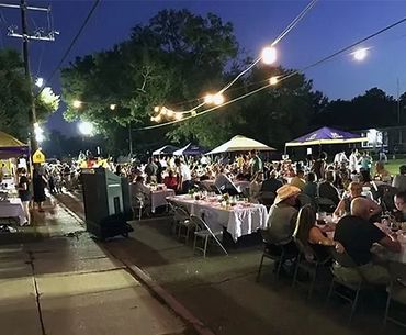 Outdoor evening gathering with string lights and people dining at tables.