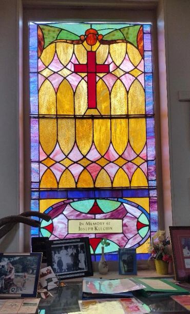 Colorful stained glass window with a red cross and memorial plaque.