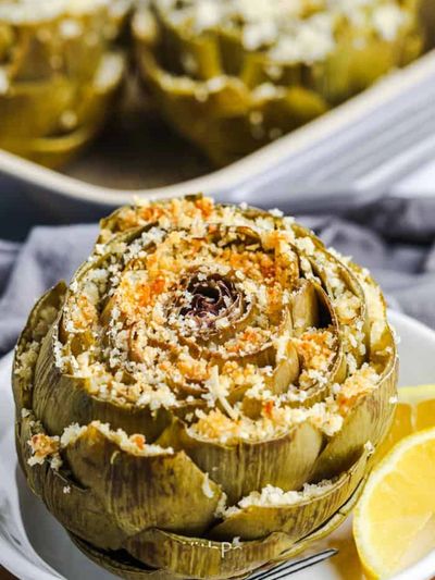 Baked artichoke topped with seasoned breadcrumbs on a white plate.
