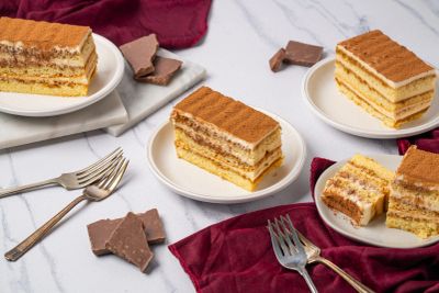 Four slices of layered cake on white plates with pieces of chocolate and forks.