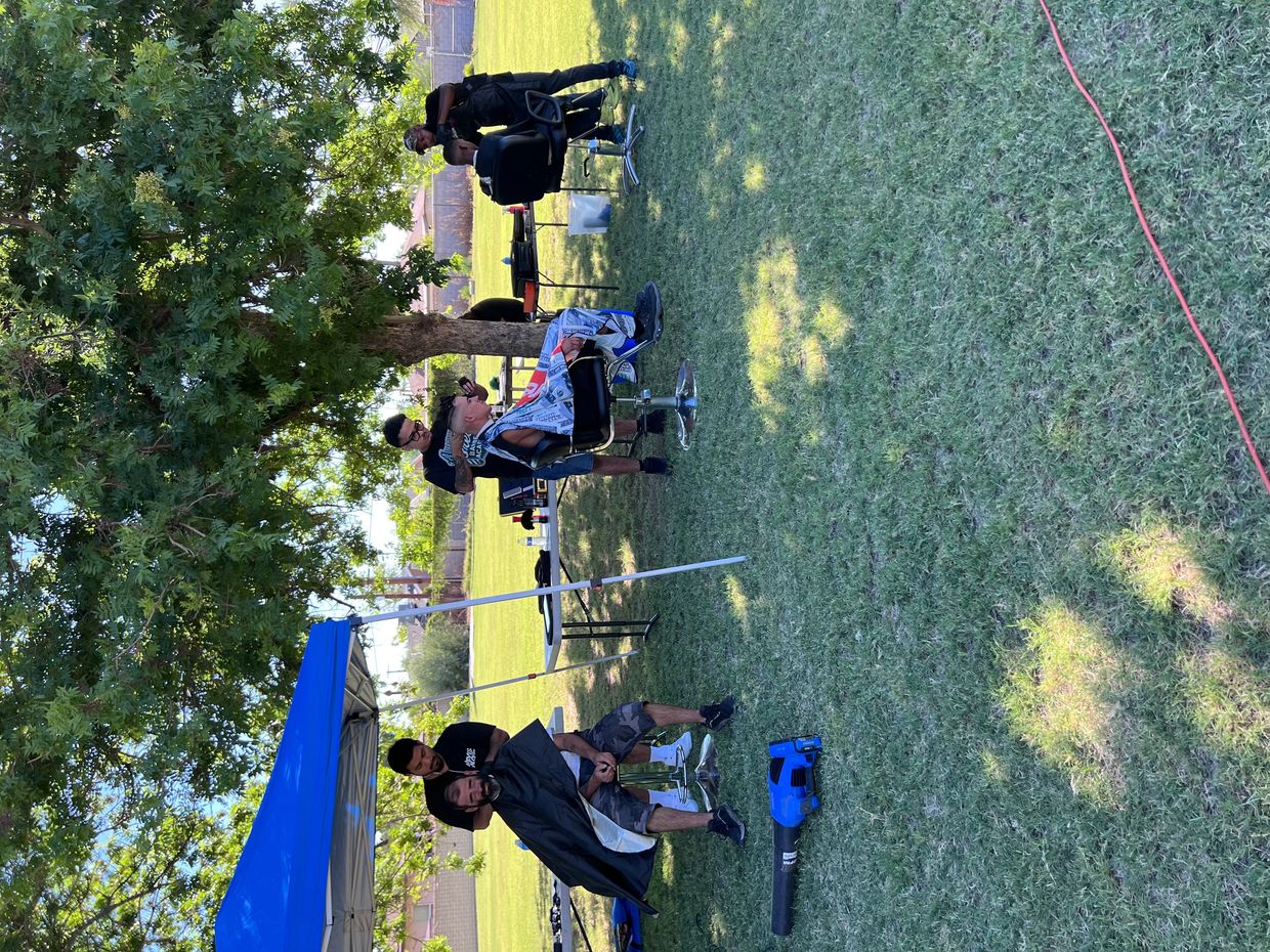 Outdoor haircut session under a tree with barbers and clients.