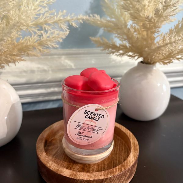 Pink scented candle on wooden base with dried plants in white vases.
