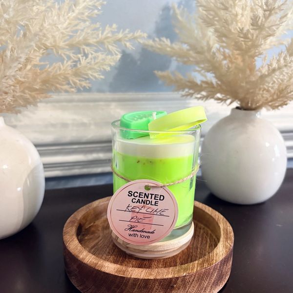 Handmade key lime pie scented candle in a glass jar on a wooden tray.