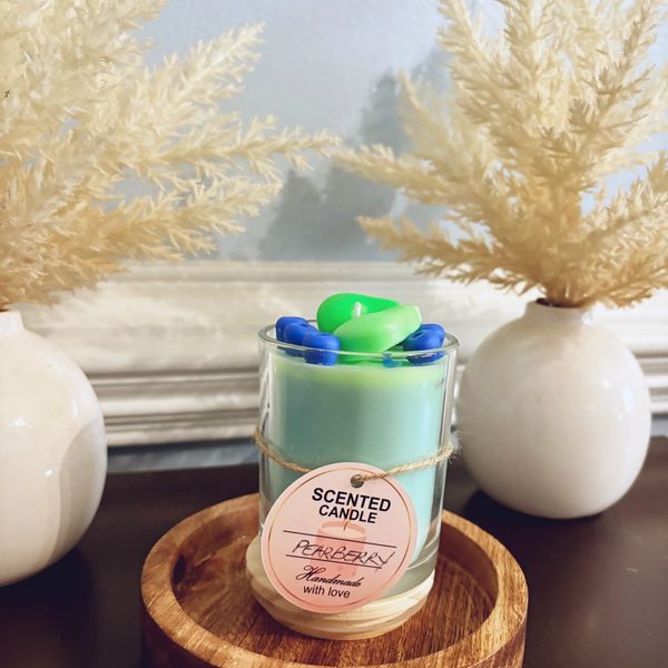 Green scented candle labeled Pearberry on a wooden tray between white vases.