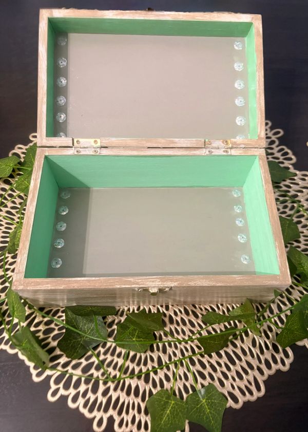 Open wooden box with green interior and decorative gems.