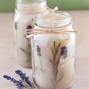 Two homemade candles in jars with lavender sprigs inside and tied with twine.