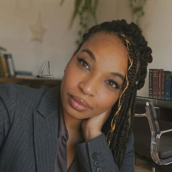 Woman with braided hair in a gray suit jacket.