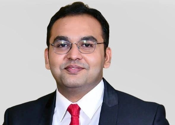 Man in formal suit with glasses and red tie smiling.