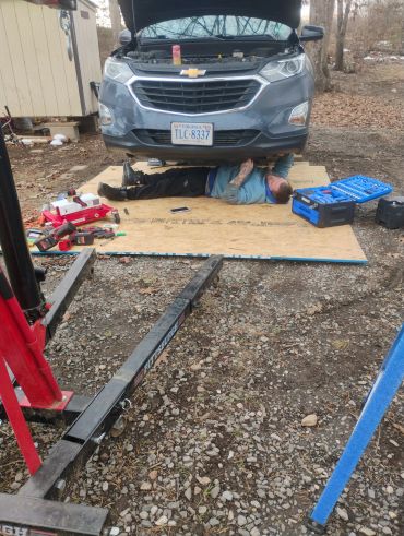 Man working under a lifted car with tools around.