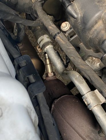 Close-up of car engine components with visible oxygen sensor.