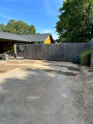 Empty driveway with wooden fence and house in background under clear sky.