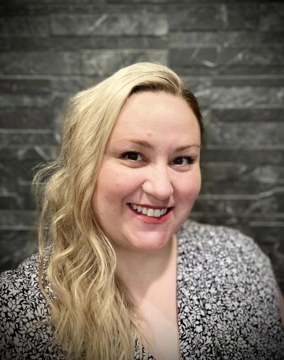 Smiling woman with long blonde hair against a stone wall.