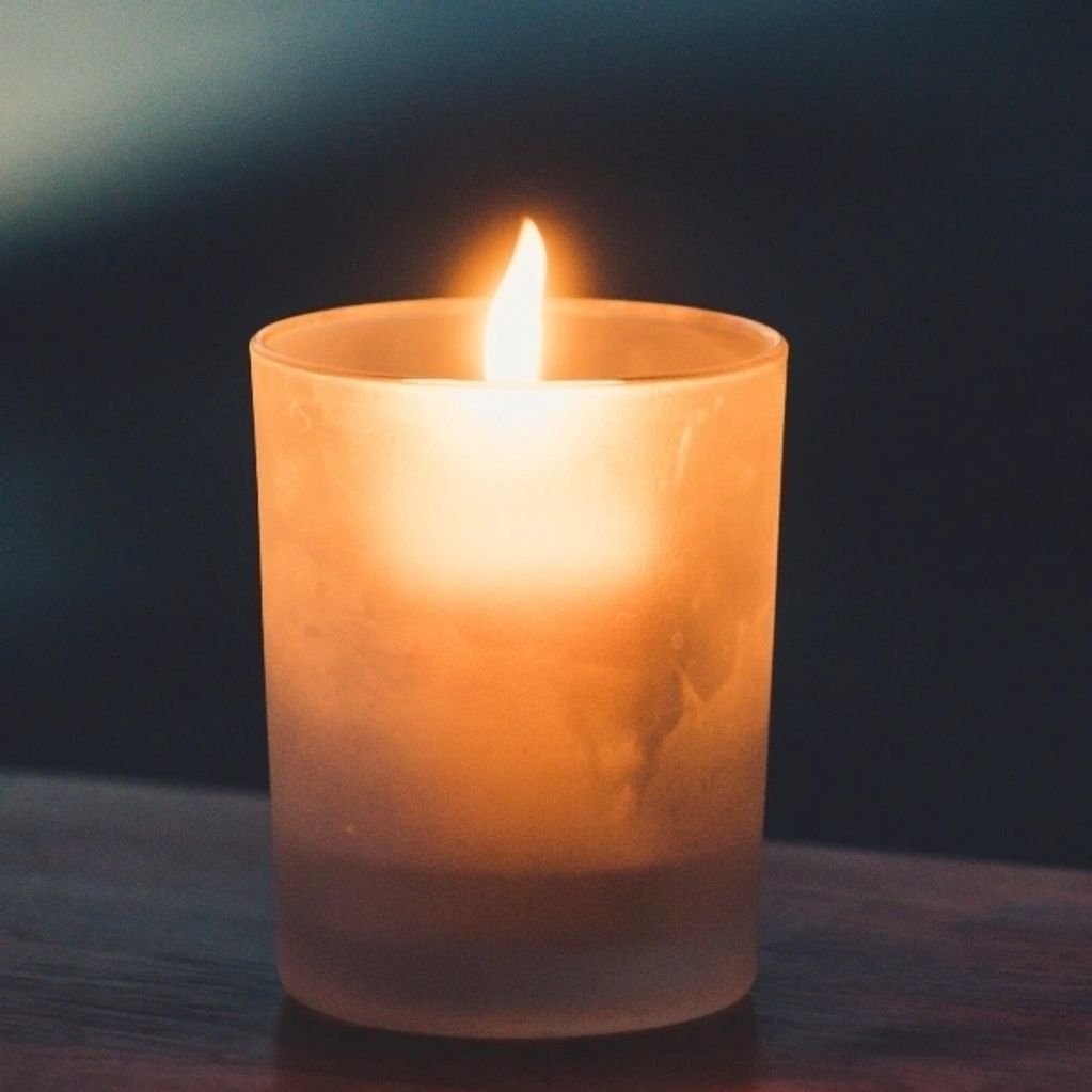 Lit candle glowing warmly inside a frosted glass holder on a dark surface.