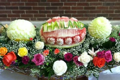 Intricately carved fruit centerpiece with the word 'THAILAND' surrounded by colorful flowers.