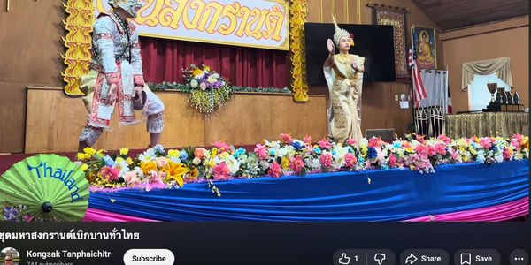 Traditional Thai dancers in elaborate costumes perform on a flower-adorned stage.