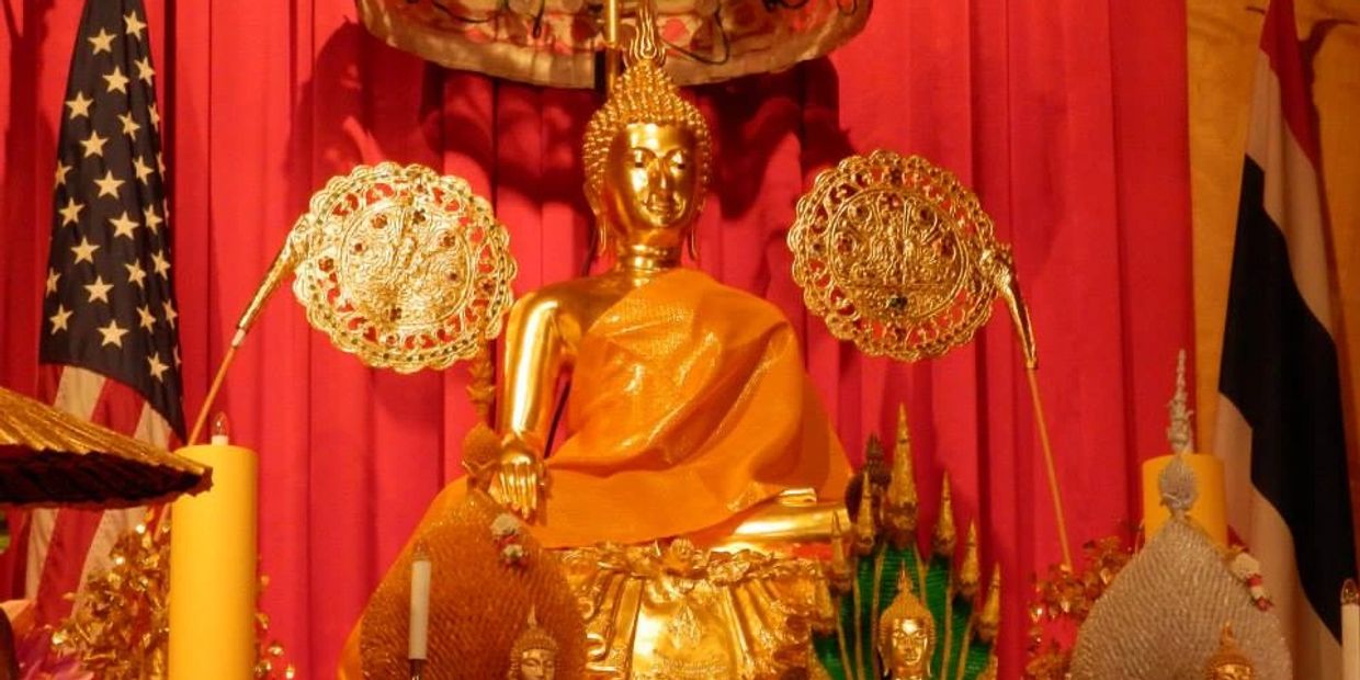 Golden Buddha statue draped in orange cloth with American and Thai flags behind.