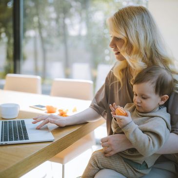 Image of a mother holding a child on her lap while working on a laptop.