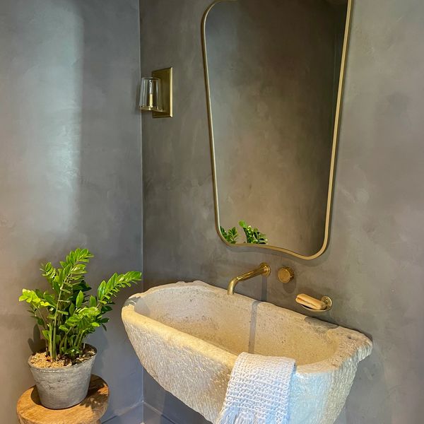 Minimalist stone sink with gold fixtures and a green plant in a modern bathroom.