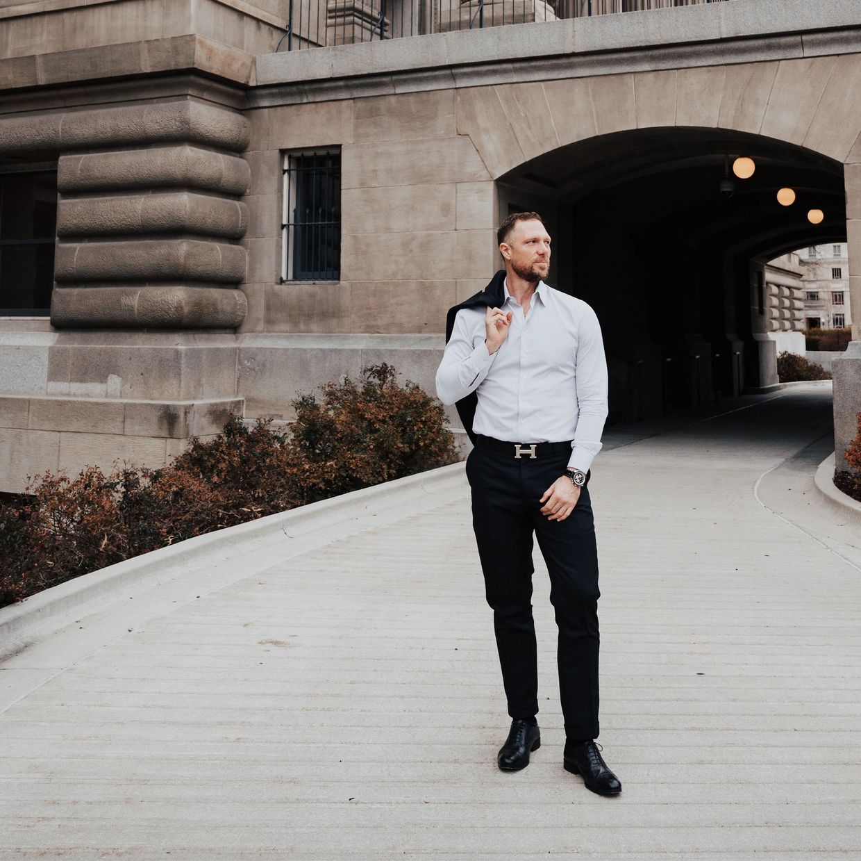 Man in formal attire walking confidently near a stone building.
