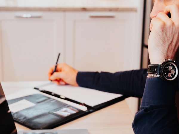 Person writing on paper while talking on phone at desk.