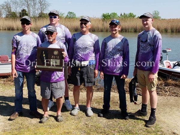 Six men in matching fishing shirts pose by a lake holding a championship plaque.