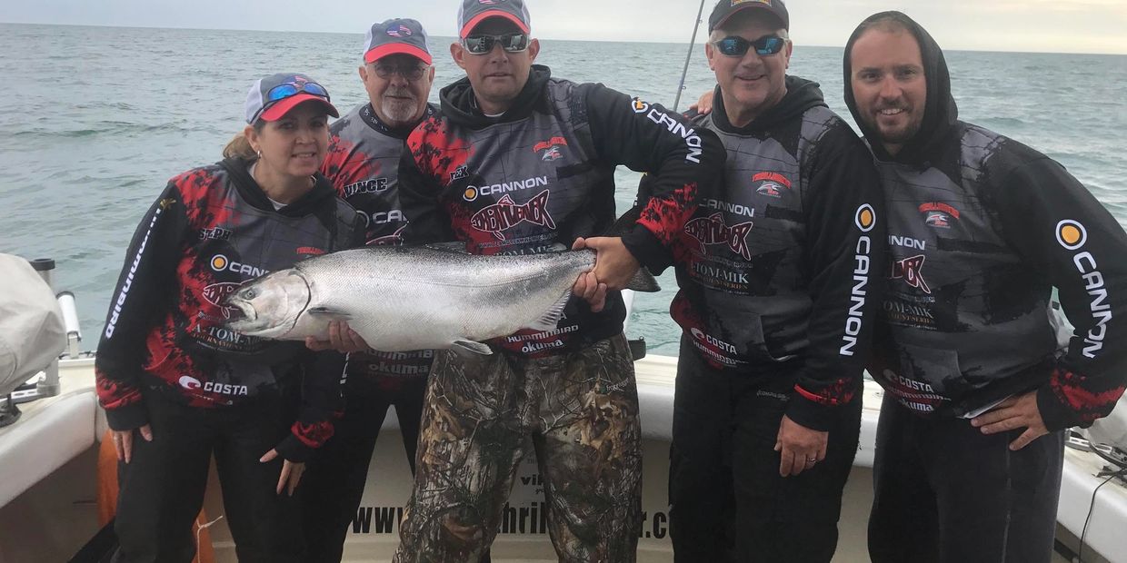 Five people on a boat proudly holding a large fish they caught.