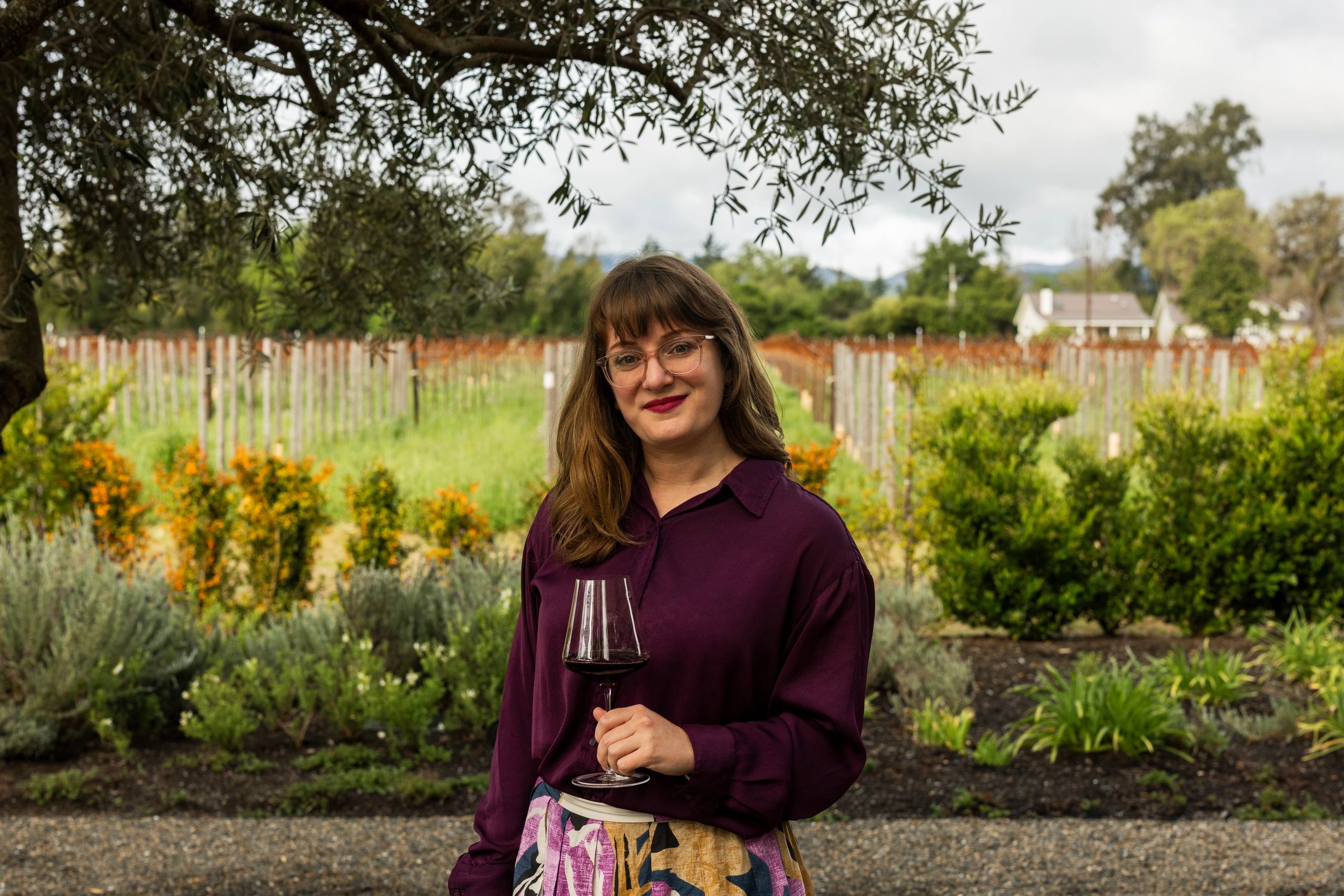 Your DTC wine sales consultant: a woman in glasses holding a glass of wine in a vineyard.
